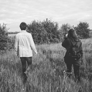 Rear view of friends walking on field against sky