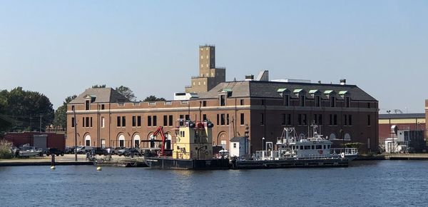 Buildings by river against clear sky