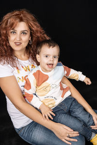 Portrait of mother and daughter sitting against black background