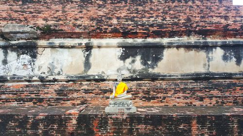 The ancient buddha sacred statue standing at the old brick wall at ayudhaya thailand.