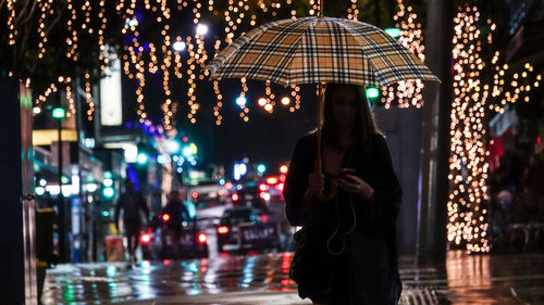 Woman standing on illuminated street during rainy season at night