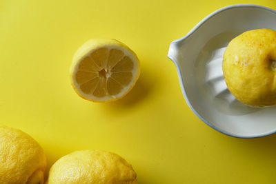 Squeezing a lemon in a white ceramic juicer on a yellow background