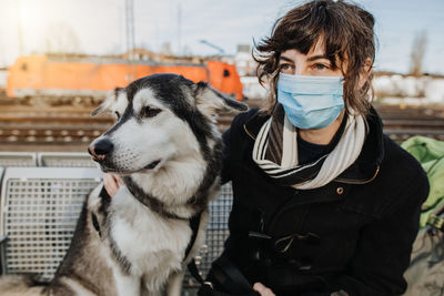 Woman wearing mask sitting with dog outdoors