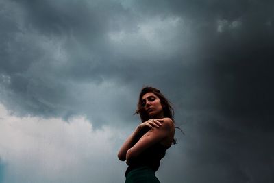 Young woman holding camera against cloudy sky
