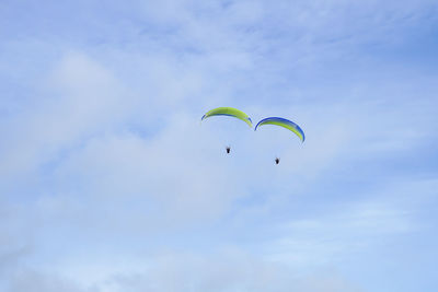 Low angle view of people paragliding against sky