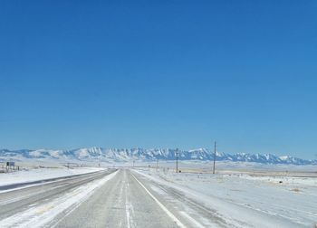 Road leading towards snowcapped mountains against clear blue sky