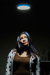 Portrait of young woman looking away while standing against black background