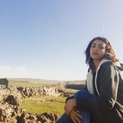 Beautiful young woman sitting on land against sky