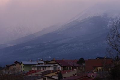 Houses by mountain against sky during winter