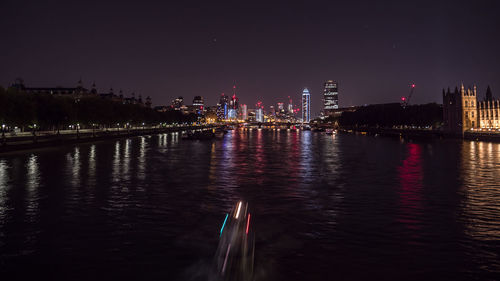Illuminated buildings by river against sky at night