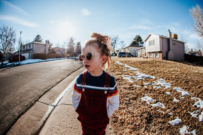 Young girl looking away standing on sidewalk in neighborhood