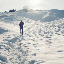 Rear view of man walking on snow covered field