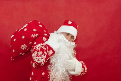 Santa holds a bag of gifts on a red background behind his back and gives a thumbs up.