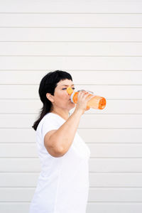 Side view of man holding drink standing against white wall