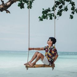 Side view of man swinging at beach against sky