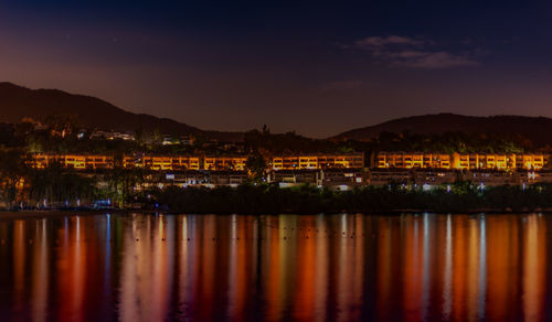 Scenic view of lake by illuminated city against sky at night
