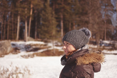 Side view of woman in warm clothing standing on snow covered field