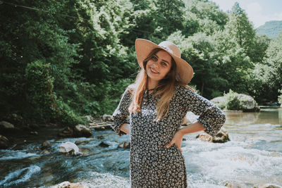 Portrait of young woman in hat standing against trees