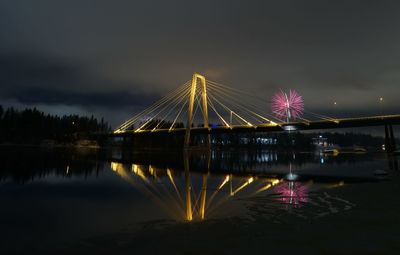 Illuminated bridge over river against sky at night