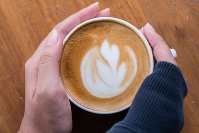 High angle view of hand holding coffee cup on table