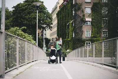 Full length of father and children walking on bridge in city