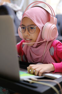 Close up of a girl in pink scarf looking at computer and having online education