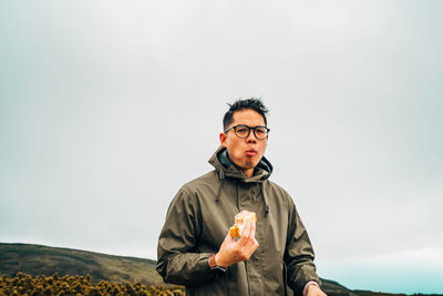 Portrait of young man eating food against sky