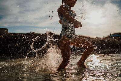 Side view of man splashing water against sky