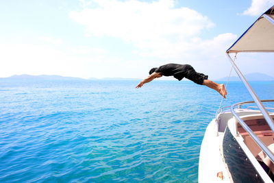 Full length of man jumping from boat in blue sea against sky