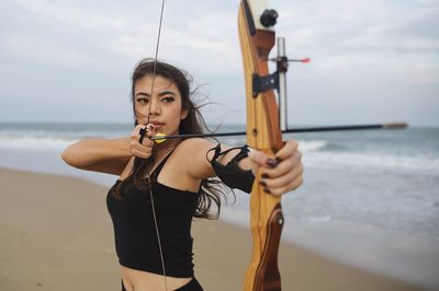 Smart young asian archery woman with bow shooting on the beach.