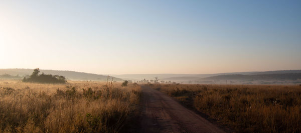 Dirt road amidst field against clear sky