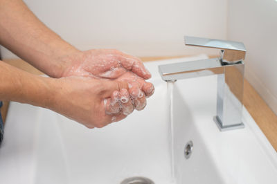 Men's hands with soap under a stream of water in the washbasin