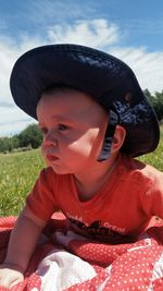 Close-up of baby wearing sun hat while lying on field against sky