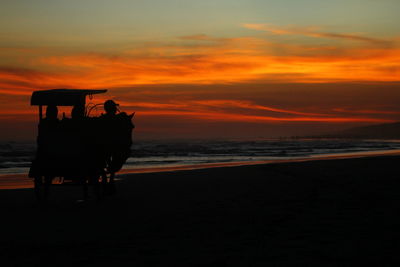 Silhouette people on beach against sky during sunset