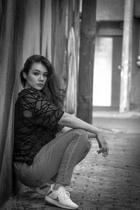 Portrait of young woman crouching by wall outdoors