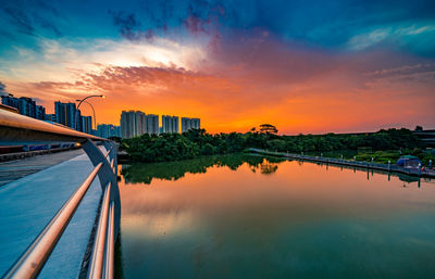 Scenic view of river by buildings against sky during sunset