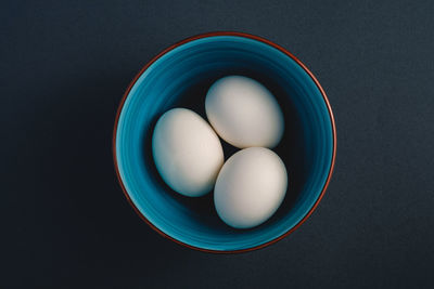 White eggs in blue bowl on dark moody black plain minimal background, happy easter day