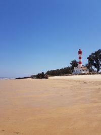 Lighthouse on beach against clear blue sky