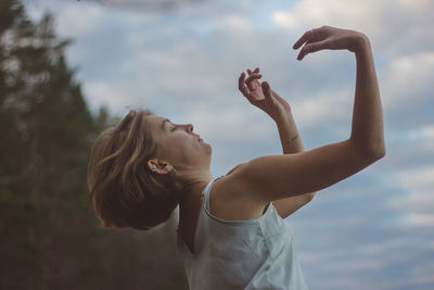 Midsection of woman standing with arms raised against sky