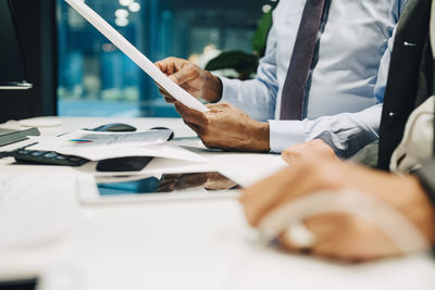 Midsection of businessman holding document in meeting at office desk