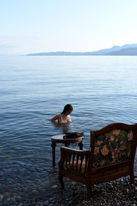 Rear view of woman sitting on bench against lake
