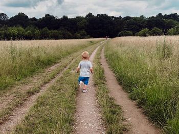 Rear view of siblings walking on footpath amidst field