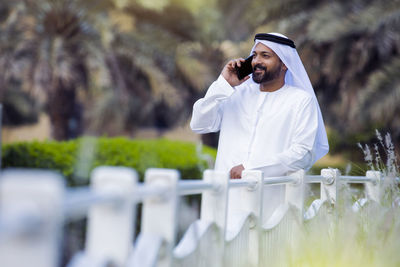 Smiling man talking on phone while standing at park