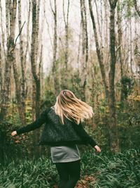 Rear view of woman walking on field in forest