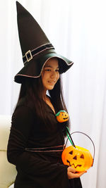 Happy girl holding hat standing against wall during halloween