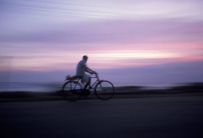 Blurred motion of man riding bicycle on road during sunset