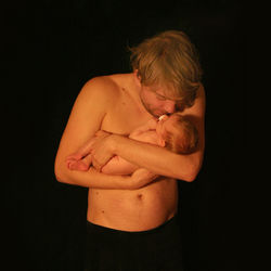 Shirtless man holding newborn baby against black background