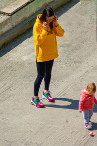 High angle view of mother talking over smart phone while standing with daughter on road