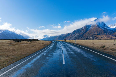 Empty road leading towards mountains against blue sky