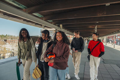 Multiracial male and female friends walking together below bridge at railroad station